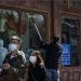 En esta imagen del 12 de abril de 2020, una pareja china camina frente a un trabajador que limpia las ventanas de una tienda de ropa donde se despliegan lineamientos para prevenir la pandemia en la reanudación de labores en Beijing. (AP Foto/Andy Wong)