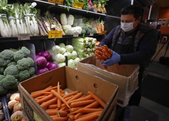 Un empeado luciendo una máscara protectora y guantes contra el COVID-19, coloca zanahorias en los estantes en el Gus's Community Market el viernes, 27 de marzo del 2020, en San Francisco.  (AP Foto/Ben Margot)