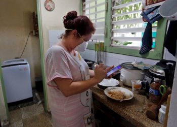 Una mujer revisa su teléfono en la cocina de su casa el 6 de abril de 2020 en La Habana. Foto: EFE/Ernesto Mastrascusa