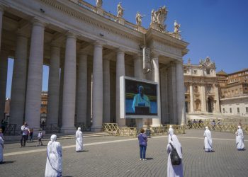 Monjas y fieles respetan el distanciamiento social mientras observan al papa Francisco recitar una oración a través de una pantalla en la plaza de San Pedro, en el Vaticano, el domingo 24 de mayo de 2020. (AP Foto/Andrew Medichini)