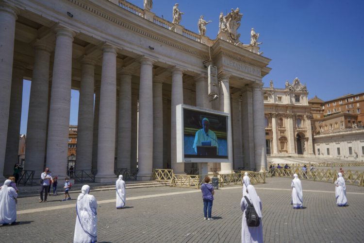Monjas y fieles respetan el distanciamiento social mientras observan al papa Francisco recitar una oración a través de una pantalla en la plaza de San Pedro, en el Vaticano, el domingo 24 de mayo de 2020. (AP Foto/Andrew Medichini)