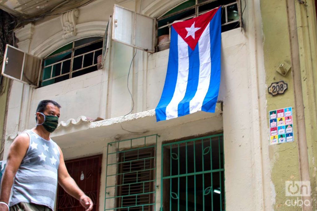 Un hombre pasa cerca de una bandera cubana colgada en una calle de La Habana, el 1 de mayo de 2020. Foto: Otmaro Rodríguez / Archivo.