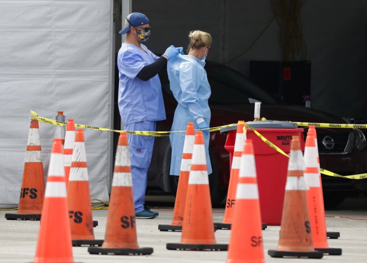 Trabajadores de la salud se ayudan mutuamente a colocarse equipo protector en un sitio de testeo del coronavirus en Miami Gardens, Florida, 5 de julio de 2020.  
Foto: Wilfredo Lee/Ap.