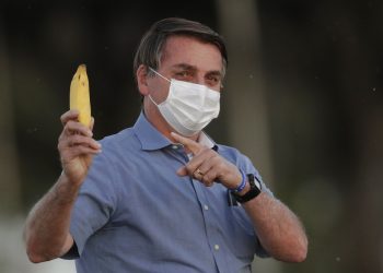 El presidente de Brasil Jair Bolsonaro señala un plátano a la prensa después de intentar dárselo de comer a un ñandú antes de iniciar la ceremonia de retiro de bandera afuera de su residencia oficial en el palacio Alvorada, en Brasilia, Brasil, el viernes 24 de julio de 2020. (AP Foto/Eraldo Peres)