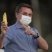 El presidente de Brasil Jair Bolsonaro señala un plátano a la prensa después de intentar dárselo de comer a un ñandú antes de iniciar la ceremonia de retiro de bandera afuera de su residencia oficial en el palacio Alvorada, en Brasilia, Brasil, el viernes 24 de julio de 2020. (AP Foto/Eraldo Peres)