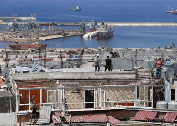 Trabajadores reparan tanques de agua dañados en departamentos con el escenario de la explosión del 4 de agosto en el puerto de Beirut al fondo, en Beirut. Foto: Hussein Malla/AP.