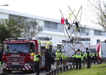 Policías y bomberos movilizados ante una imprenta de Broxbourne, donde varios manifestantes bloquean la carretera con una estructura, en Broxbourne, Hertfordshire, Inglaterra, el sábado 5 de septiembre de 2020. Foto: Yui Mok/PA via AP.