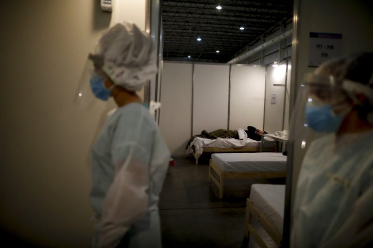 Trabajadores sociales caminan por habitación donde una persona con COVID-19 descansa dentro del Parque Tecnopolis, reutilizado como refugio para pacientes con COVID-19 que están asintomáticos o tienen síntomas leves, en Buenos Aires. Foto/Natacha Pisarenko/AP.