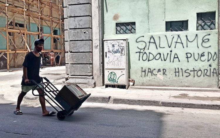 Un joven con nasobuco lleva un televisor en una carretilla, en La Habana. Foto: Ernesto Mastrascusa / EFE.