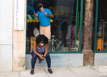 Una mujer revisa su teléfono móvil en las afueras de una tienda que se prepara para su reapertura, tras la flexibilización de las restricciones por la COVID-19 en La Habana. Foto: Otmaro Rodríguez.