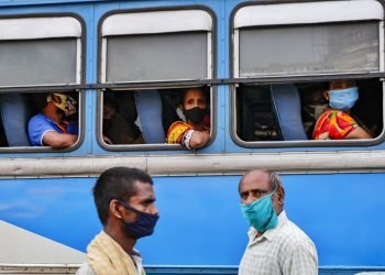 Pasajeros, con mascarilla para protegerse del coronavirus, esperan en el interior de un autobús mientras dos peatones cruzan por delante, en una estación de buses en Calcuta, India, el 1 de octubre de 2020. Foto: AP Foto/Bikas Das.