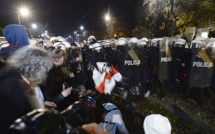 La policía arranca un cartel mientras manifestantes se concentran frente a la residencia del dirigente oficialista polaco Jaroslaw Kaczynski para protestar un fallo de la Corte Constitucional que endurece las leyes contra el aborto.  Foto: Czarek Sokolowski/AP.