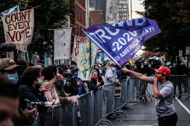 Un seguidor del presidente Trump ondea una bandera frente a un grupo de seguidores de Joe Biden en el exterior de un centro de escrutinio electoral en Filadelfia. Foto: Mario Cruz / EFE