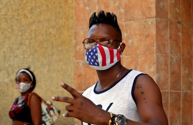Un joven usa una mascarilla con diseño de la bandera de Estados Unidos, mientras posa para una foto en La Habana. Foto: Ernesto Mastrascusa / EFE.