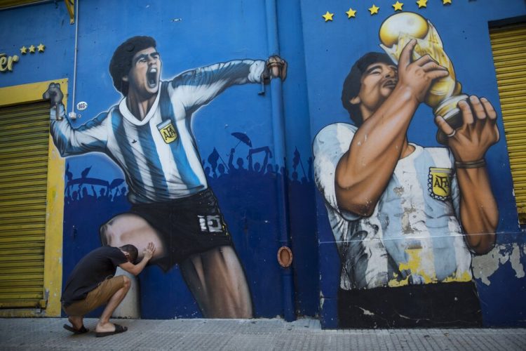 Augusto Canosa reza al tocar una pintura de Diego Maradona cerca del estadio La Bombonera de Boca Juniors en Buenos Aires, Argentina, el viernes 27 de noviembre de 2020. Foto: AP/Rodrigo Abd.