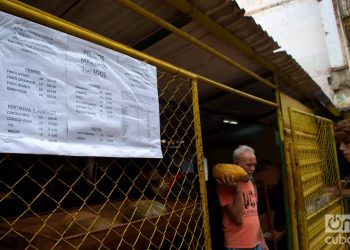 Un hombre sale con sus compras de un mercado agropecuario en La Habana. En primer plano, el listado de precios "topados" por el gobierno. Foto: Otmaro Rodríguez/Archivo OnCuba.