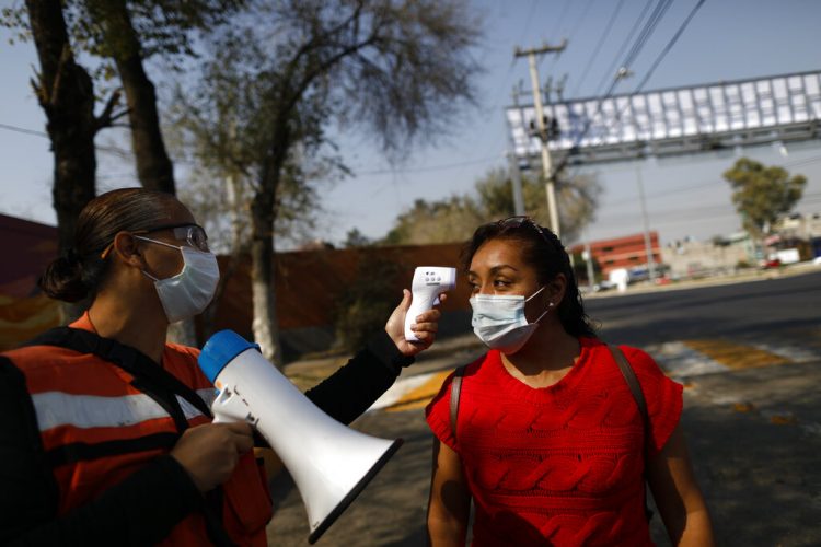 Trabajadora le toma la temperatura a una mujer con la intención de reducir la propagación del coronavirus, en las inmediaciones del mercado Central de Abastos. Foto: Rebecca Blackwell/AP.