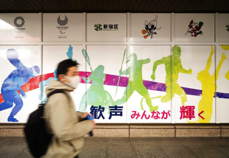 Un hombre con mascarilla pasa frente al edificio de oficinas municipales de Shinjuku, en el que se promocionan los Juegos Olímpicos reprogramados para mediados de este año, en Tokio, el viernes 29 de enero de 2021. Foto: AP/Hiro Komae.