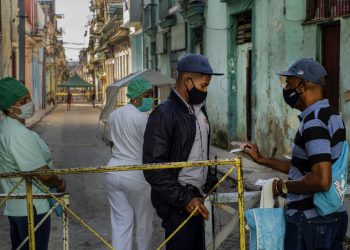 Un residente muestra su identificación a un oficial de policía que está limitando el acceso a un vecindario como una forma de frenar la propagación de la pandemia de COVID-19, mientras enfermeras están detrás en La Habana, Cuba, el lunes 22 de febrero de 2021. Foto: AP/Ramon Espinosa.