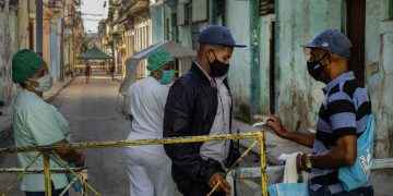 Un residente muestra su identificación a un oficial de policía que está limitando el acceso a un vecindario como una forma de frenar la propagación de la pandemia de COVID-19, mientras enfermeras están detrás en La Habana, Cuba, el lunes 22 de febrero de 2021. Foto: AP/Ramon Espinosa.