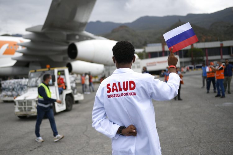 Un trabajador de la salud sostiene una bandera nacional rusa mientras es descargado un cargamento de la vacuna rusa Sputnik V contra el COVID-19, en el Aeropuerto Internacional Simón Bolívar en Maiquetía, Venezuela, el sábado 13 de febrero de 2021  Foto: Matías Delacroix/Ap.