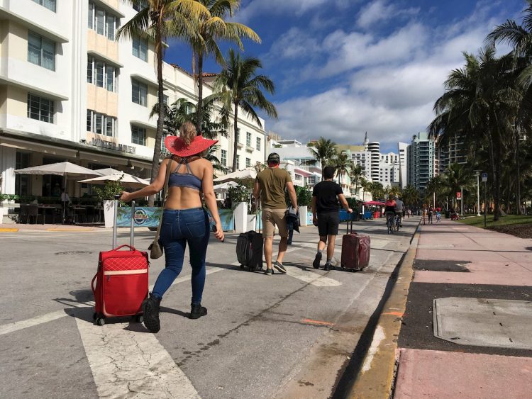 Varias personas caminan con su equipaje a través de la avenida Ocean Drive, en Miami Beach, Florida, luego de decretarse el toque de queda nocturno por sus autoridades. Foto: Ivonne Malaver / EFE.