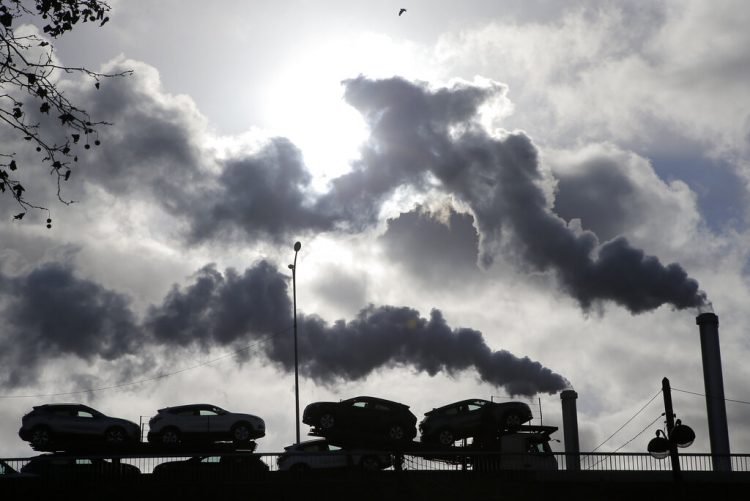 Humo saliendo de una fábrica mientras un camión cargado de autos pasa por un puente en París, Francia.  Foto: Michel Euler/Ap/ Archivo.