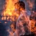 Un trabajador municipal con EPI visto tras las llamas de una de las hogueras prendidas en un crematorio para víctimas de la covid-19, este viernes en Bombay, India. Foto: EFE/ Divyakant Solanki.