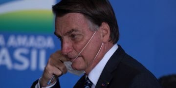 El presidente de Brasil, Jair Bolsonaro, se quita una mascarilla en un acto en el Palacio do Planalto, en la ciudad de Brasilia. Foto: Joédson Alves / EFE.