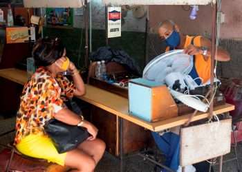 Una mujer espera que un mecánico le repare un ventilador, en un taller de equipos electrodomésticos en La Habana. Foto: Yander Zamora / EFE.