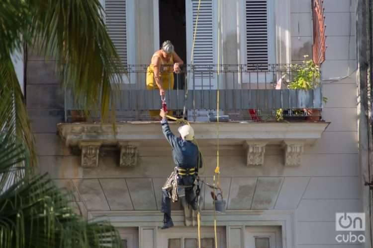 Una mujer alcanza un pomo de agua a un pintor de edificios, La Habana, Cuba. Foto: Otmaro Rodríguez.