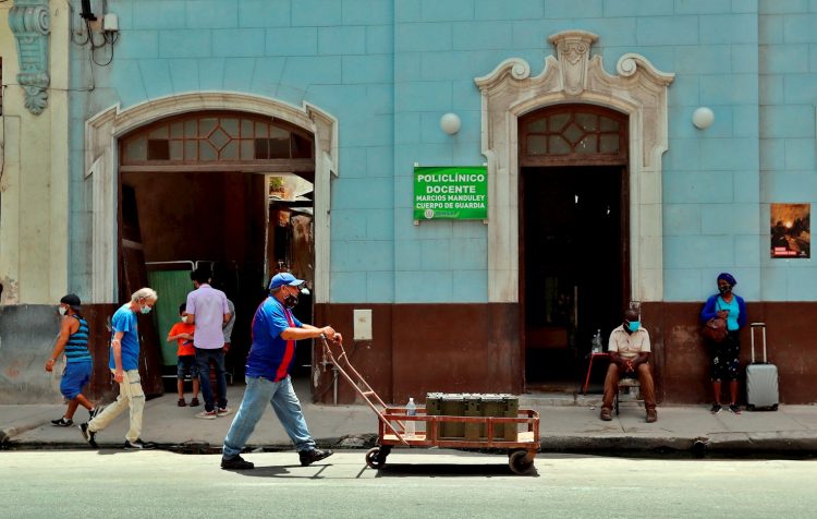 Un hombre mientras camina con una carretilla frente a un policlínico en La Habana, provincia con una de las tasas de incidencias más bajas al cierre de mes. Foto: Ernesto Mastrascusa/Efe.