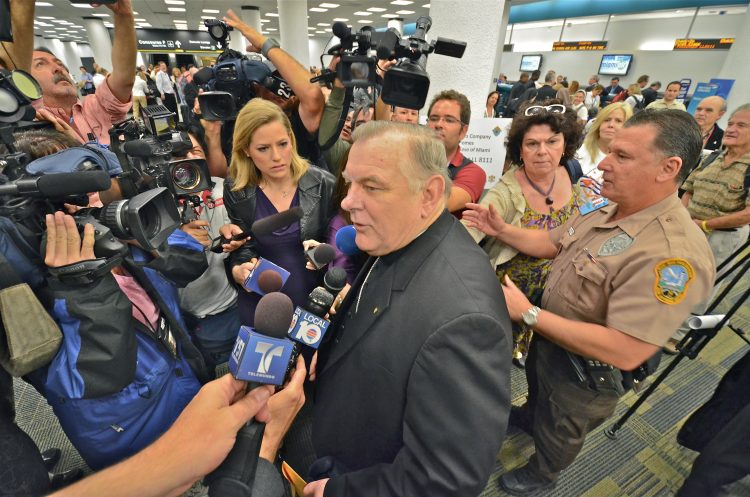 El arzobispo de Miami, Thomas Wenski, presta declaraciones en el aeropuerto de Miami, protegido por la policía local, momentos antes de partir hacia La Habana para asistir a la visita del papa Benedicto XVI a la Isla (2012). Foto: Rui Ferreira