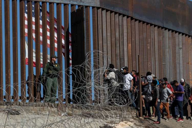 Migrantes centroamericanos miran a través de la valla mientras un agente de la Patrulla Fronteriza vigila cerca del cruce fronterizo de El Chaparral en Tijuana, México (2018). Foto: tomada de The New York Times.
