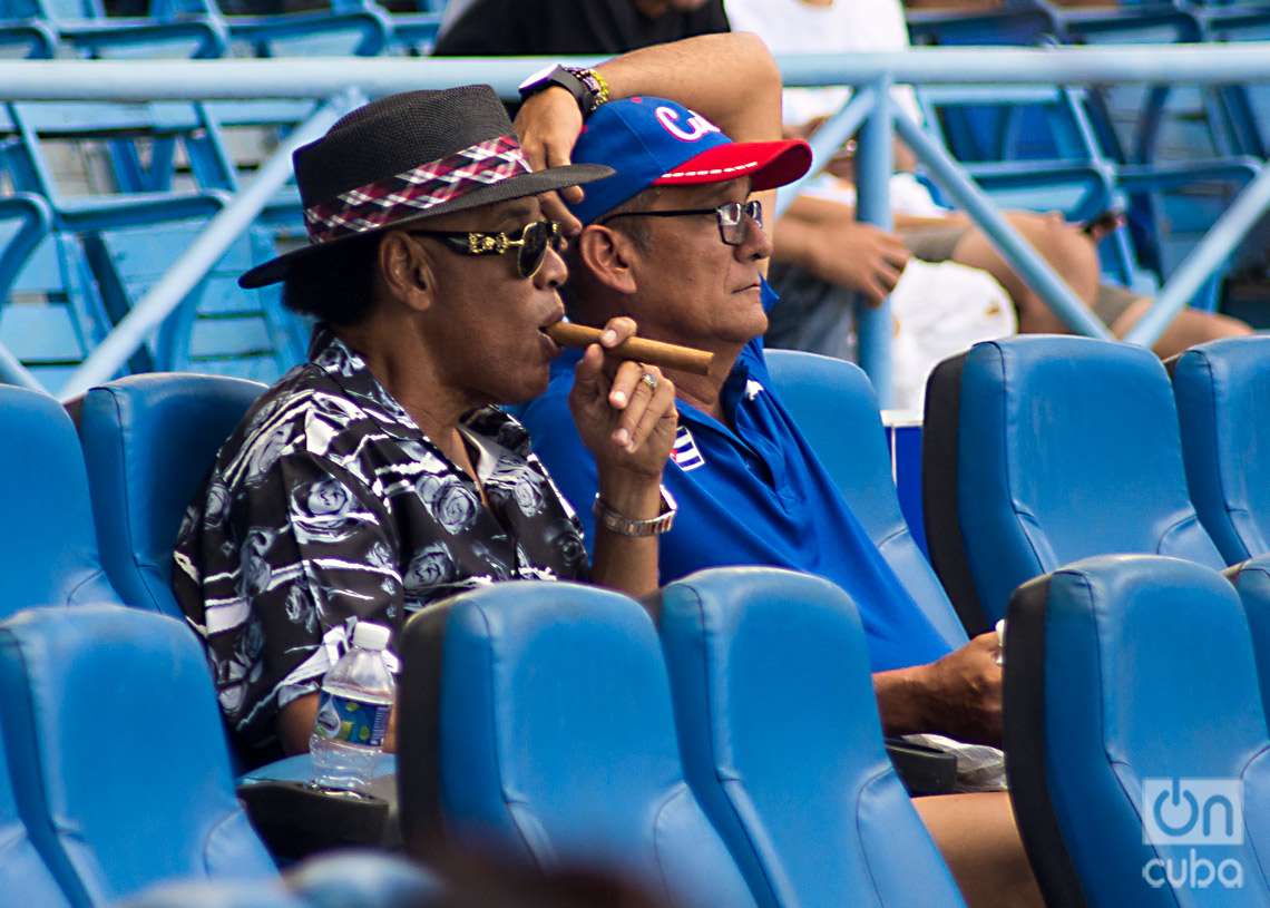 Victor Mesa, estelar exjugador y director del béisbol cubano (con sombrero y tabaco), asiste como espectador al primer partido de la I Liga Élite del Béisbol Cubano, en el Estadio Latinoamericano de La Habana. Foto: Otmaro Rodríguez.