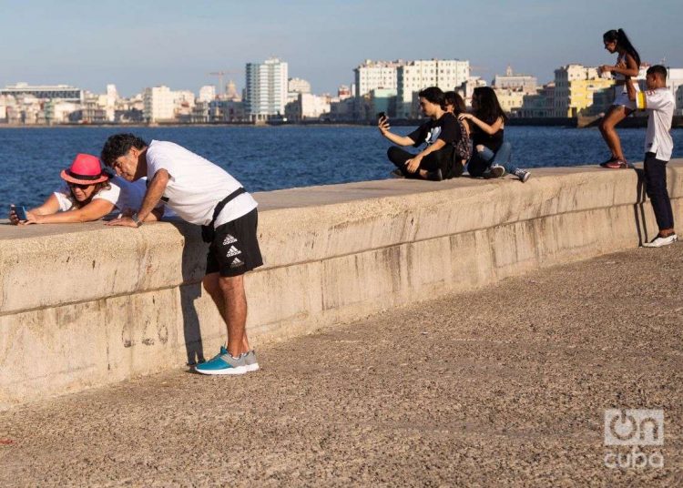 Personass se toman fotos selfie en el malecón de la Habana en 2022 Ciudad al fondo, mar. Foto: Jorge Ricardo