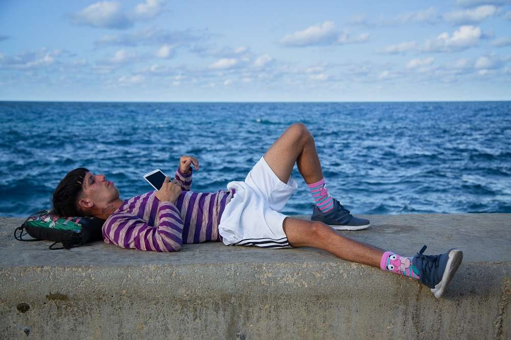 joven muchacho acostado sobre el muro del malecón de la habana con celular frente al mar foto jorge ricardo