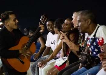 Grupo de personas en el muro del malecón de la Habana escucha a un músico aficionado con su guitarra de noche. Foto: Jorge Ricardo