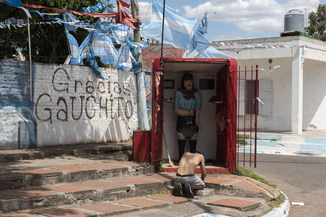 Un hombre arrodillado frente a la figura del Gauchito Gil, personaje de devoción religiosa en Argentina.