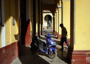 Hombre camina junto a una moto eléctica en un pórtico de La Habana, Cuba, 2023. Foto: Alejandro Ernesto.