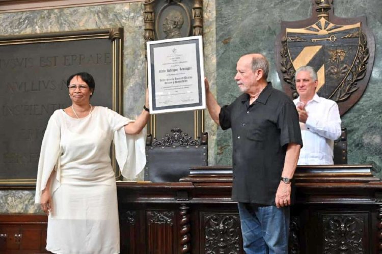 La rectora de la Universidad de La Habana, Miriam Nicado, entre el título de Doctor Honoris Causa al trovador Silvio Rodríguez. Detrás, el presidente cubano Miguel Díaz-Canel. Foto: @PresidenciaCuba / Twitter.