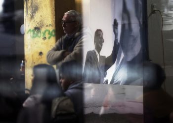 Imagen del expresidente Salvador Allende reflejada en un vidrio entre personas que visitan el museo de memoria en el Estadio Nacional, el 26 de agosto 2023, en Santiago de Chile. Foto:  Elvis González/EFE.