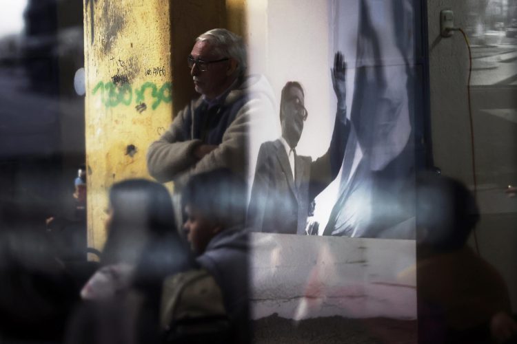 Imagen del expresidente Salvador Allende reflejada en un vidrio entre personas que visitan el museo de memoria en el Estadio Nacional, el 26 de agosto 2023, en Santiago de Chile. Foto:  Elvis González/EFE.