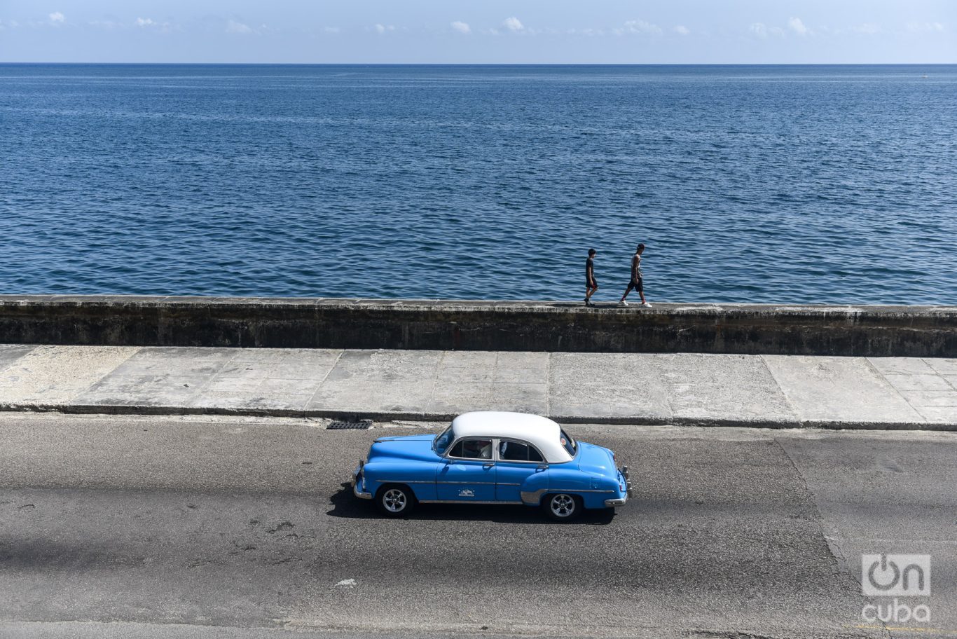 Dos hombres caminan por el muro del malecón de la habana mientras un auto americano recorre la calle, La Habana Cuba, 2023 Foto: Kaloian.