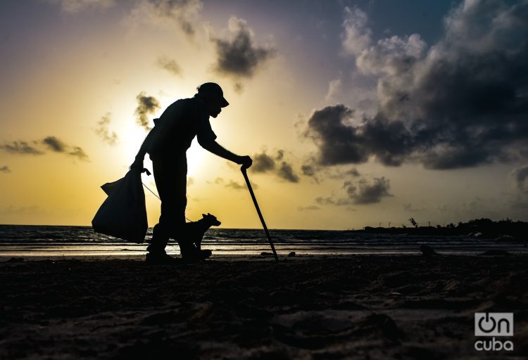 Un anciano con su perro caminan al amanecer por la playa recolectando latas. Foto: Kaloian.