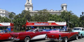 Varios autos clásicos junto a un ómnibus esperan la llegada de turistas para ofrecerles sus paseos por La Habana. Foto: Ernesto Mastrascusa / EFE.