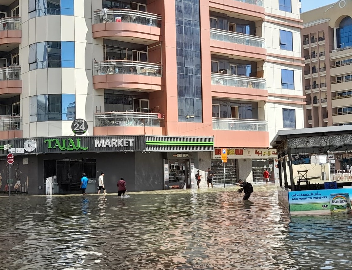 Personas en una calle inundada en el barrio de Al Barsha, días después de las torrenciales lluvias caídas en Dubái. Foto: OnCuba.