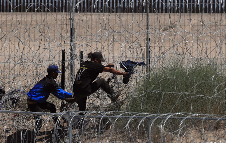 Migrantes ilegales intentan cruzar por una barricada de alambre con púas en las inmediaciones de la frontera con Estados Unidos y México. Foto: Luis Torres / EFE.