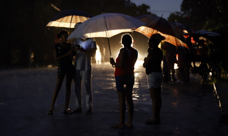 Persona esperan bajo la lluvia la reconexión de la electricidad. Foto: Ernesto Mastrascusa/ EFE.