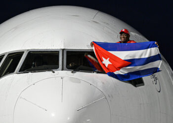 El luchador cubano Mijaín López, cinco veces campeón olímpico, sostiene una bandera de Cuba en la ventanilla del piloto a su llegada este lunes al aeropuerto José Martí de La Habana luego de participar en los Juegos Olímpicos de París 2024. Foto: Adalberto Roque / POOL / AFP vía EFE.